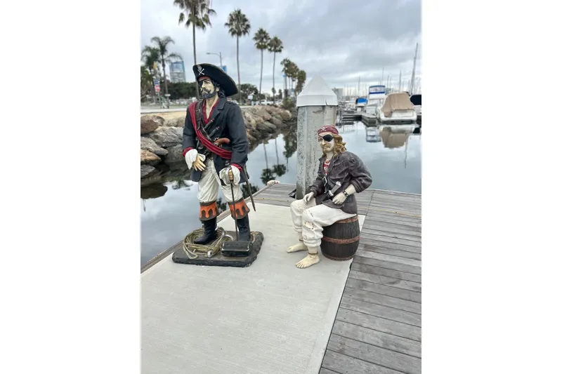 Slide: The Image of Pirate statues on dock with boats and palm trees in background, Custom Brigantine 1977. - 17