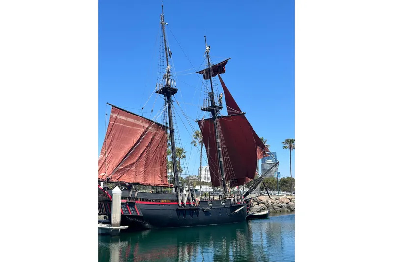 Slide: The Image of Vintage 1977 Custom 80 Brigantine ship with red sails docked in a sunny harbor. - 3
