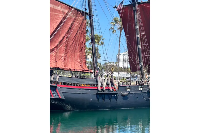 Slide: The Image of Vintage 1977 Custom 80 Brigantine ship with red sails docked near palm trees. - 5