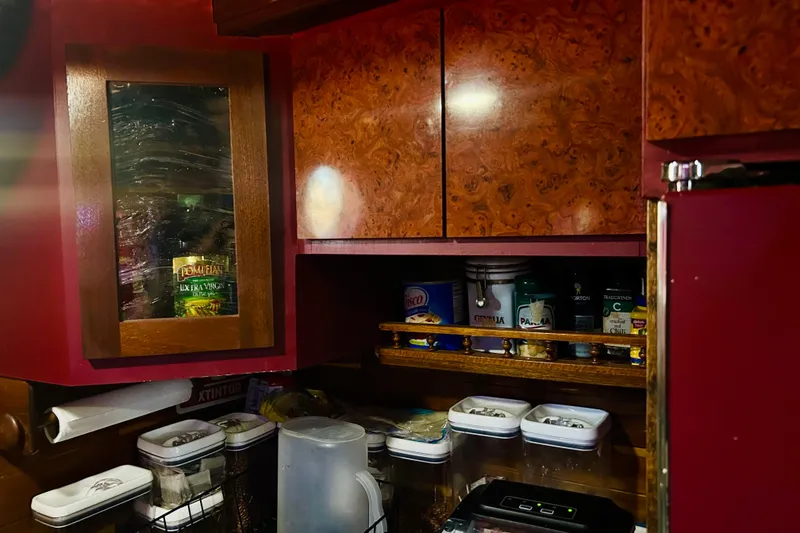 Slide: The Image of Kitchen storage in a 1977 Custom Brigantine, featuring wooden cabinets and various pantry items. - 42