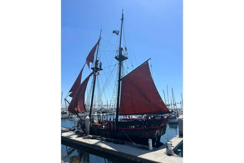 Slide: The Image of Vintage 1977 Custom 80 Brigantine sailboat docked with red sails under clear blue sky. - 2