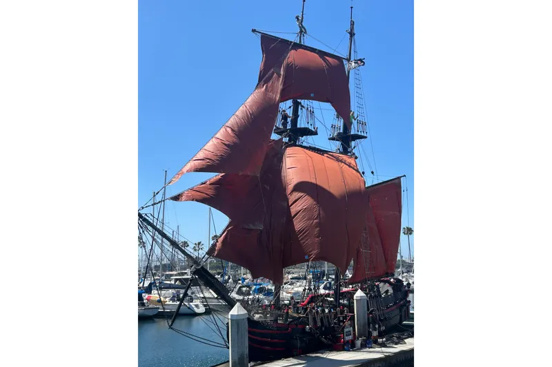 Slide: The Image of Vintage 1977 Custom 80 Brigantine ship with red sails docked at a marina. - 1