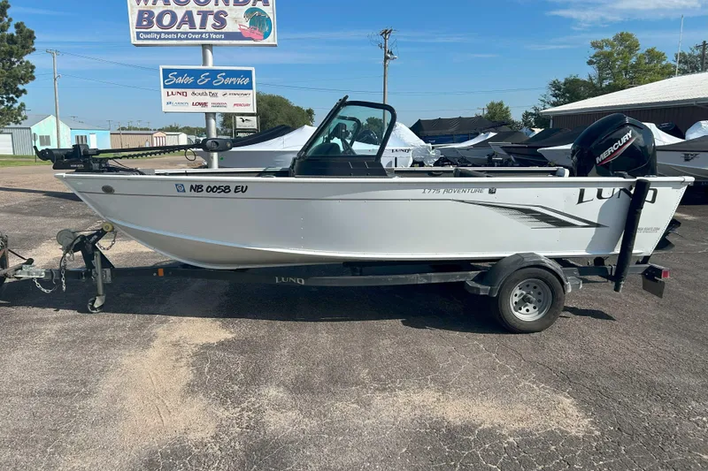 Slide: The Image of 2023 Lund 1775 Adventure Sport boat on trailer at dealership, featuring Mercury outboard motor. - 7