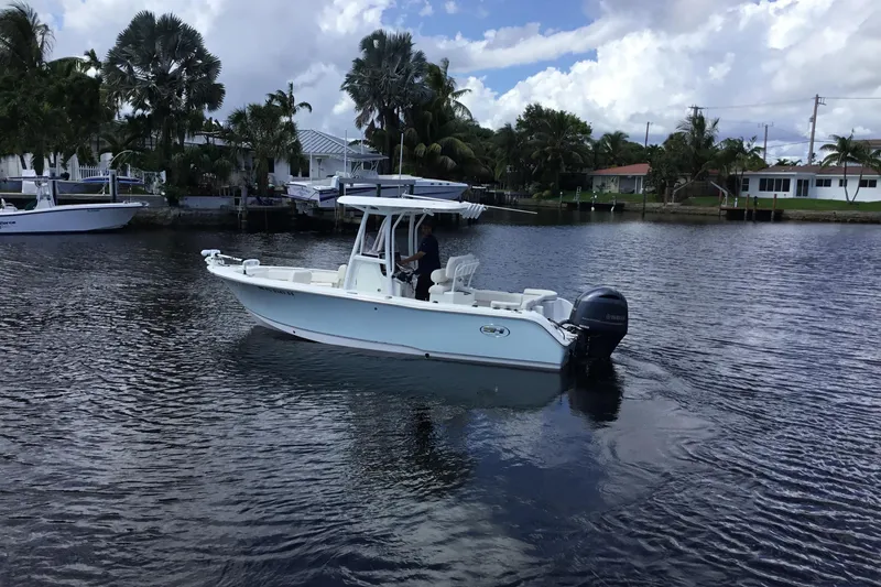 Slide: The Image of 2020 Sea Hunt Ultra 225 boat on a calm waterway with palm trees and houses. - 11