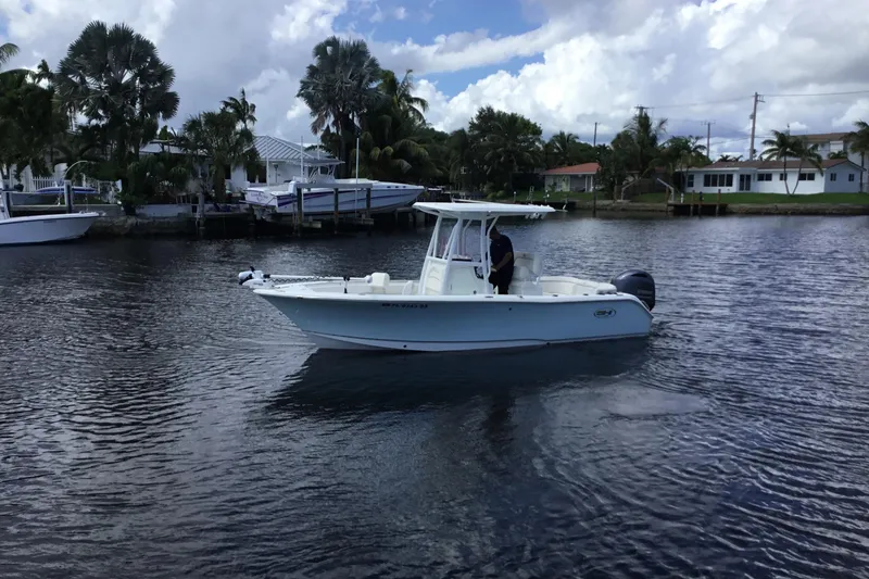Slide: The Image of 2020 Sea Hunt Ultra 225 boat cruising on a calm waterway with palm trees in the background. - 12