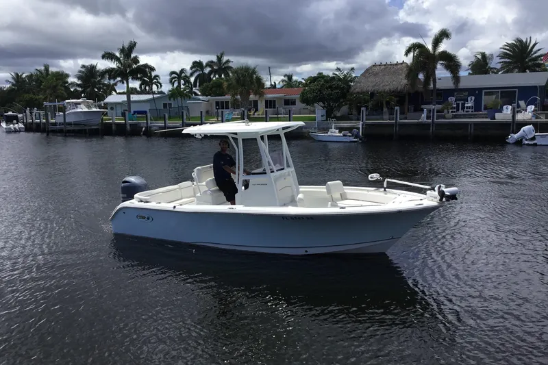 Slide: The Image of 2020 Sea Hunt Ultra 225 boat on a calm waterway with palm trees in the background. - 5