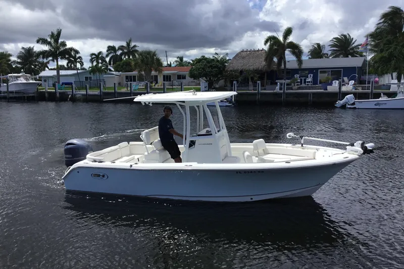 Slide: The Image of 2020 Sea Hunt Ultra 225 boat cruising on a calm waterway with palm trees in the background. - 6
