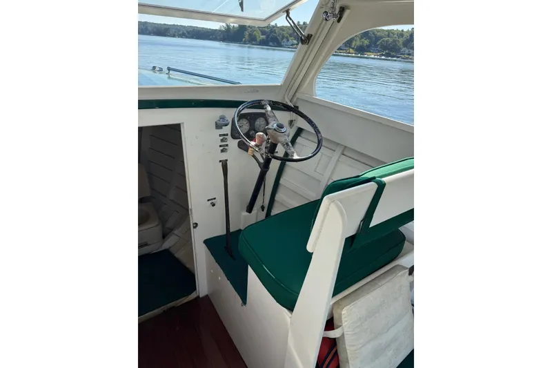 Slide: The Image of 1940 Chris-Craft Launch 25 boat interior with green seating and steering wheel, on a calm lake. - 13