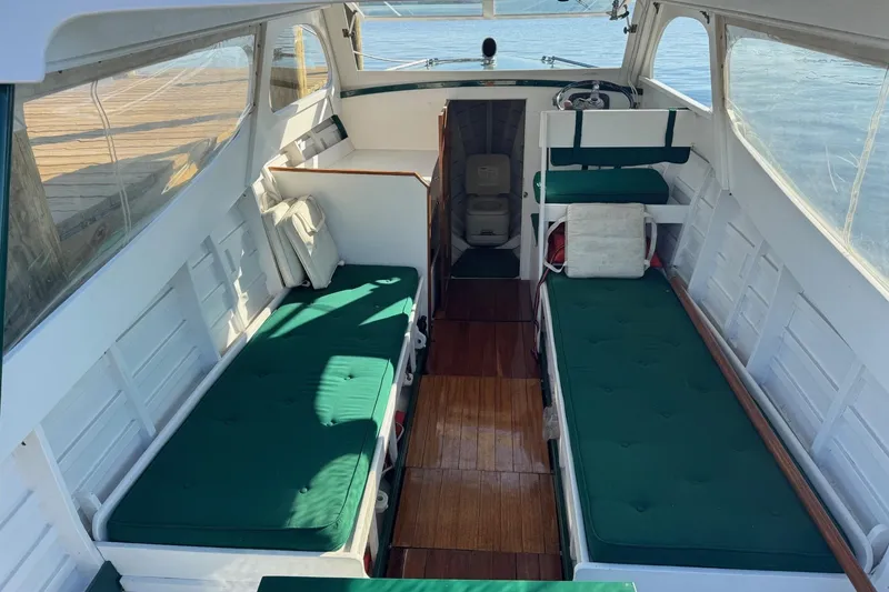 Slide: The Image of 1940 Chris-Craft Launch 25 interior with green cushions and wooden flooring, docked by the water. - 16