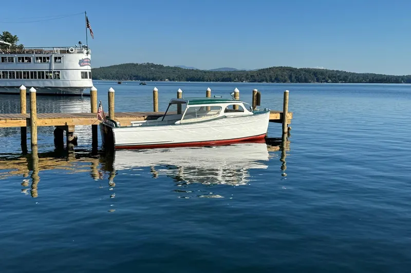Slide: The Image of 1940 Chris-Craft Launch 25 docked on a serene lake with a distant ferry. - 6