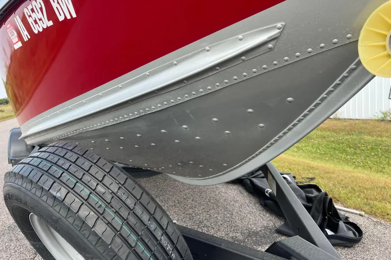 Slide: The Image of 2023 Alumacraft Voyageur 175 SC boat on trailer, showcasing red hull and tire detail. - 47