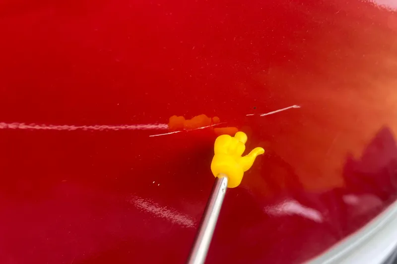 Slide: The Image of Yellow tool applying sealant on red Alumacraft Voyageur 175 SC boat surface, 2023 model. - 50