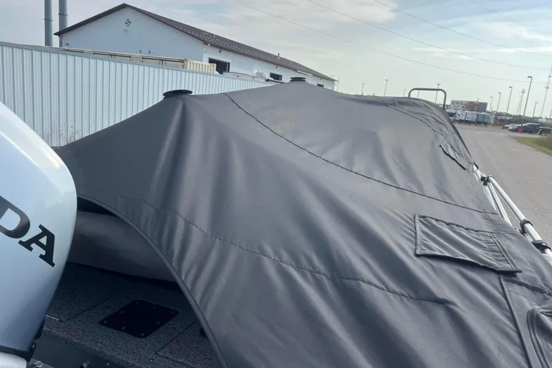 Slide: The Image of 2023 Alumacraft Voyageur 175 SC boat with protective cover, parked near industrial buildings. - 56