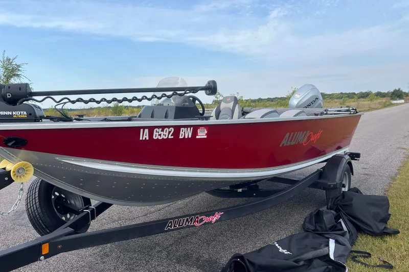 Slide: The Image of 2023 Alumacraft Voyageur 175 SC boat on trailer, red exterior, parked on roadside. - 7