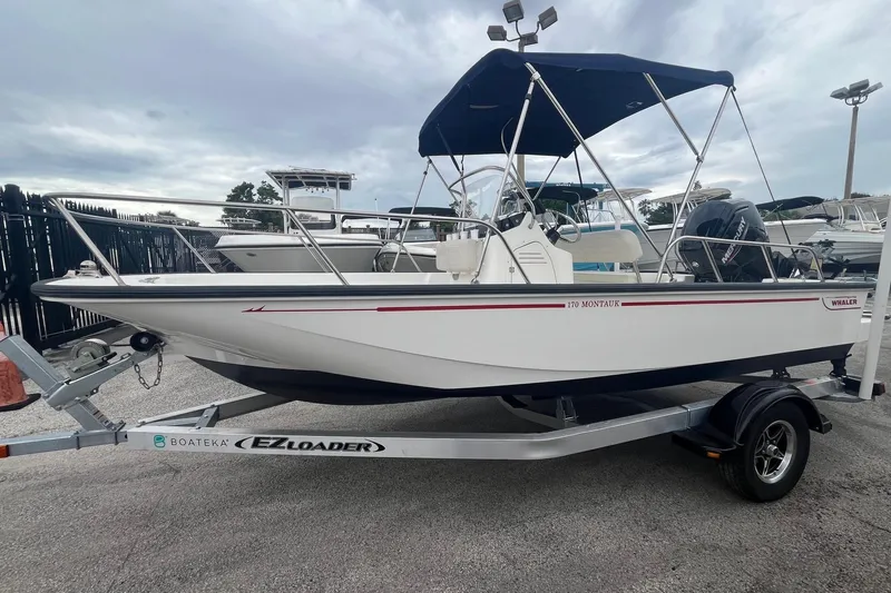 Slide: The Image of 2022 Boston Whaler 170 Montauk boat on trailer with blue canopy, parked outdoors. - 3