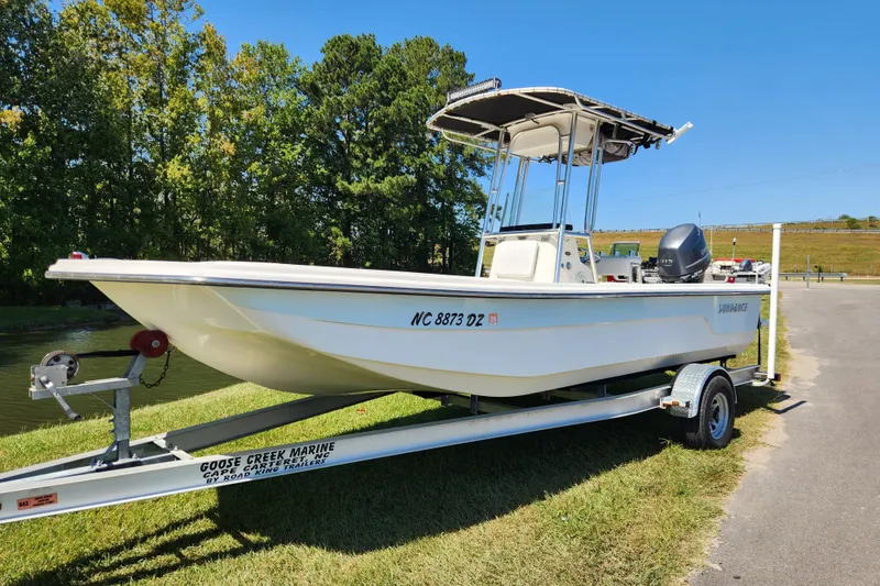 Slide: The Image of 2014 Sundance B22CC boat on trailer, parked near a grassy area with trees. - 1