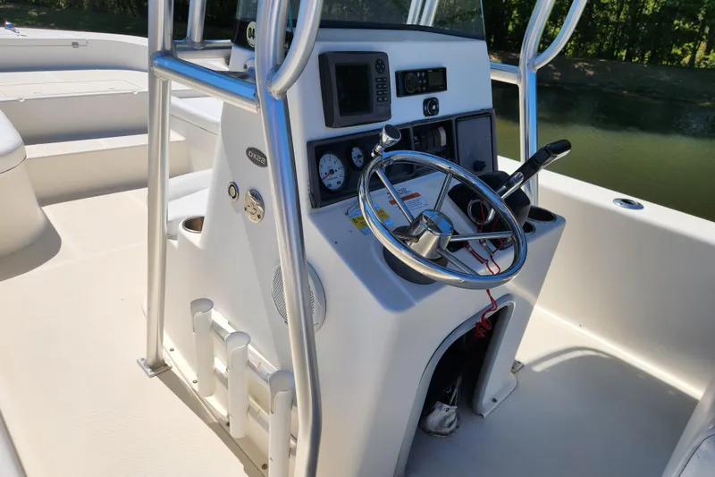 Slide: The Image of 2014 Sundance B22CC boat console with steering wheel and controls, docked by a calm waterway. - 12