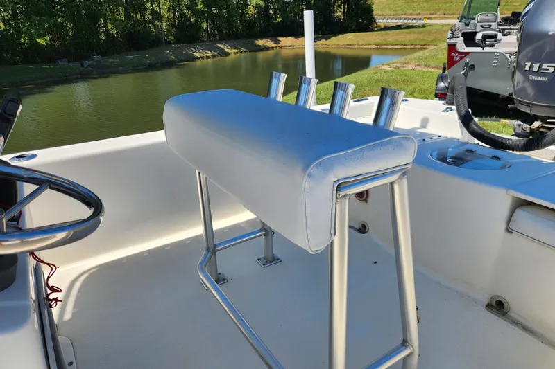 Slide: The Image of 2014 Sundance B22CC boat interior with cushioned seat and rod holders by a serene lake. - 13