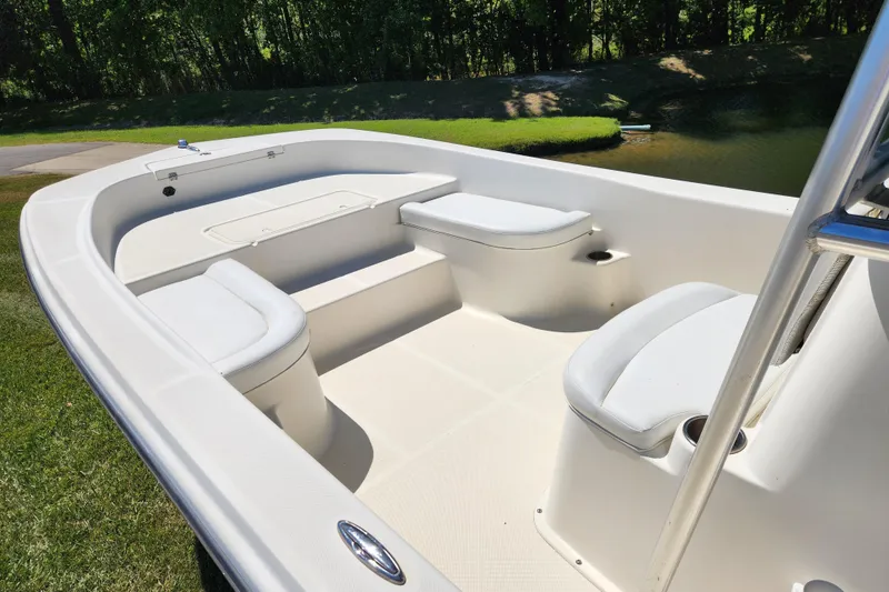 Slide: The Image of 2014 Sundance B22CC boat interior with white seating, set against a lush green backdrop. - 7