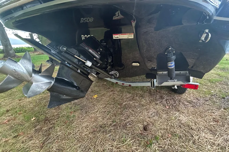 Slide: The Image of 2017 Stingray 235 LR boat stern with propeller and trailer on grassy area. - 3