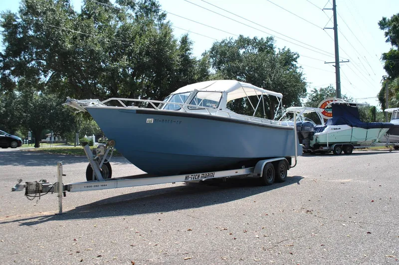 Slide: The Image of Custom 2009 model 24 boat on trailer in parking lot, surrounded by trees. - 2