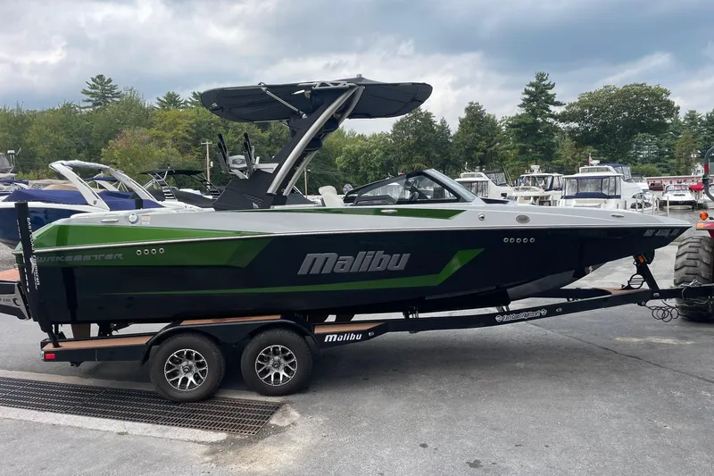 Slide: The Image of 2023 Malibu Wakesetter 24 MXZ boat on trailer, green and black design, parked outdoors. - 2