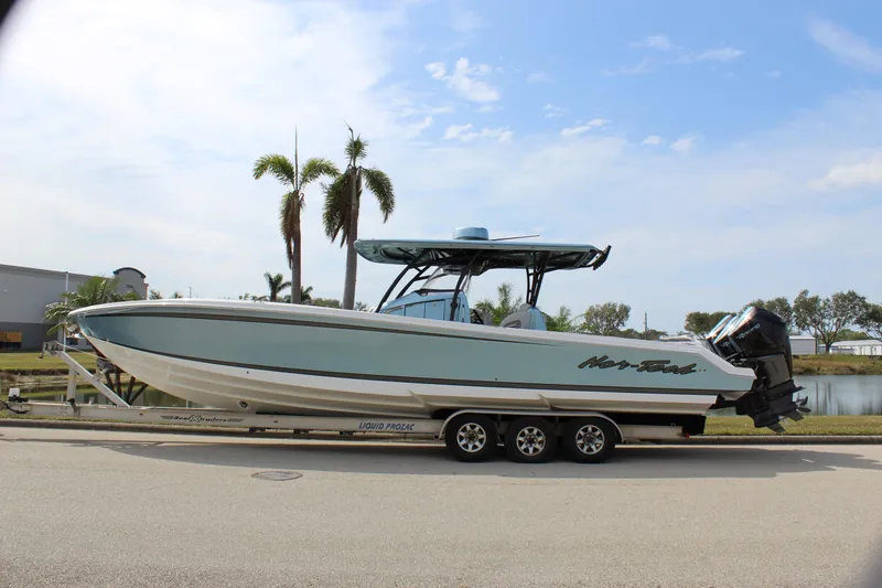 Slide: The Image of 2021 Nor-Tech 390 Sport Center Console boat on trailer, parked near palm trees. - 6