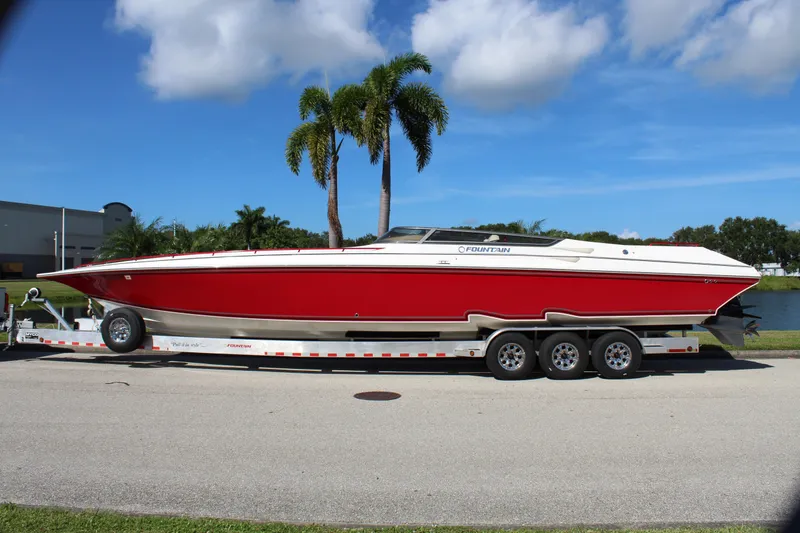 Slide: The Image of Red 2007 Fountain 42 Lightning speedboat on trailer, parked near palm trees and water. - 2