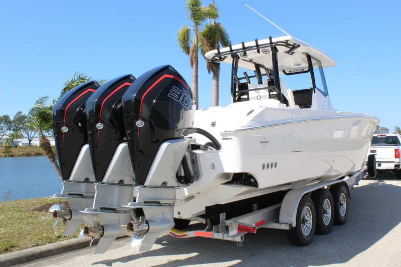 Slide: The Image of 2024 Fountain 32 NX boat on trailer with triple outboard engines, parked near water. - 21