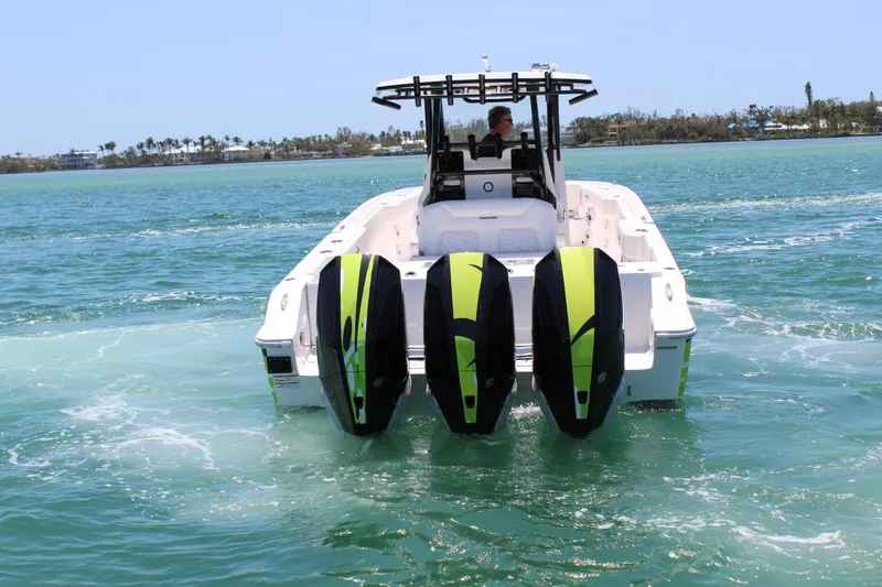 Slide: The Image of 2024 Fountain 32 NX boat with triple outboard engines cruising on clear blue water. - 7