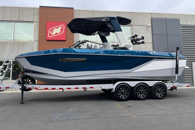 The Image of 2026 Nautique Super Air Nautique G25 boat on trailer, parked outside dealership. - 1