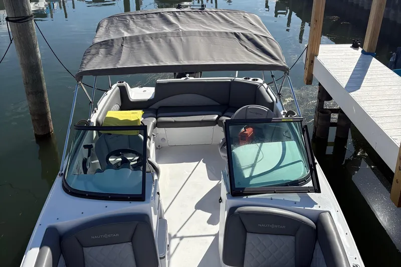 Slide: The Image of 2026 NauticStar 223 DC Deck boat docked, featuring spacious seating and canopy. - 2