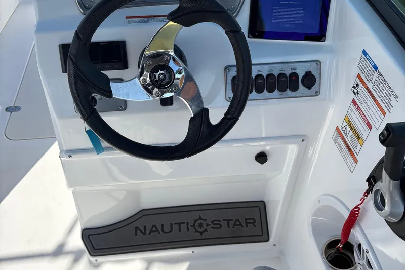 Slide: The Image of Steering console of 2026 NauticStar 223 DC Deck boat with control panel and safety warnings. - 7