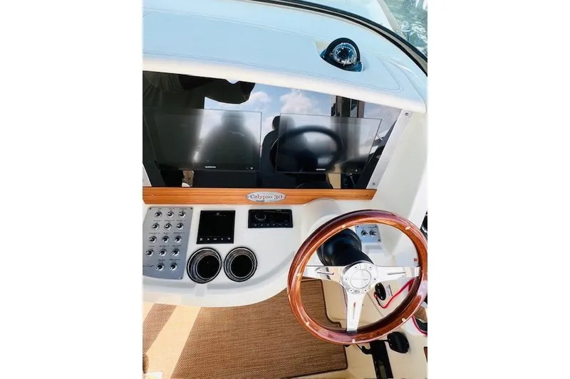 Slide: The Image of 2022 Chris-Craft Calypso 30 dashboard with wooden steering wheel and modern controls. - 26