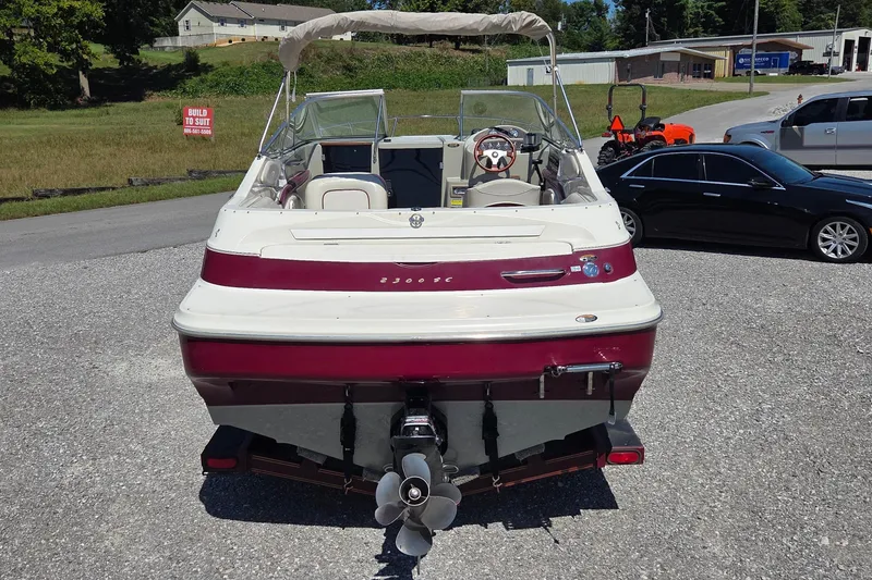 Slide: The Image of 1998 Maxum 2300 SC boat, rear view, parked on gravel with cars and buildings nearby. - 3