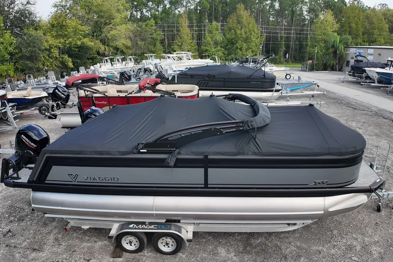 Slide: The Image of 2026 Viaggio Lago X22U pontoon boat with black cover on trailer, surrounded by other boats. - 1