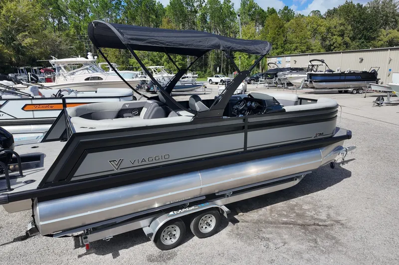 Slide: The Image of 2026 Viaggio Lago X22U pontoon boat with canopy, parked on a trailer in a marina. - 5