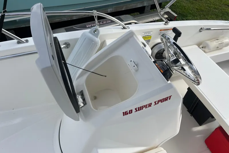 Slide: The Image of 2024 Boston Whaler 160 Super Sport boat interior with open storage compartment and steering wheel. - 8