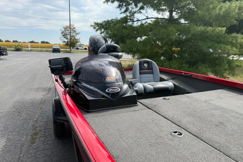 Slide: The Image of 2018 Triton 18 TX boat with red trim, parked near trees and open field. - 7