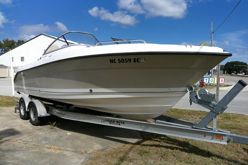Slide: The Image of 2015 Pursuit DC 235 Dual Console boat on trailer, parked outdoors under blue sky. - 1