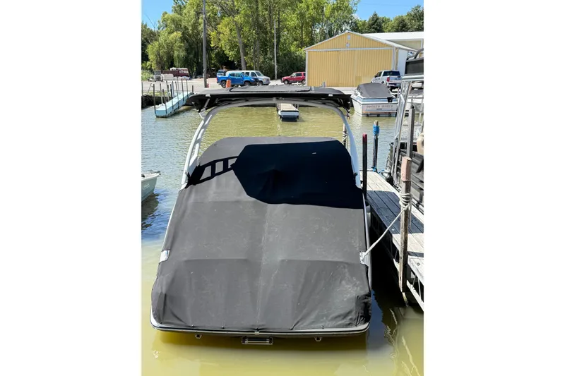 Slide: The Image of 2023 Yamaha Boats 252SD covered at dock, surrounded by calm water and trees. - 1