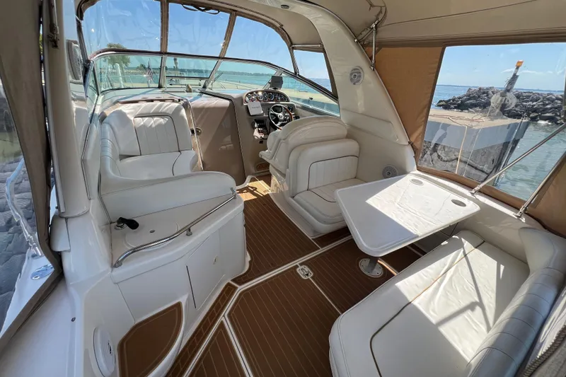 Slide: The Image of 2001 Sea Ray 290 Sundancer interior with white seating and wooden flooring, docked by the water. - 7