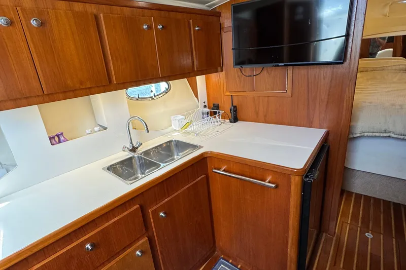Slide: The Image of Interior of 2000 Tiara Yachts 3500 Express, featuring a compact kitchen with wood cabinetry. - 32