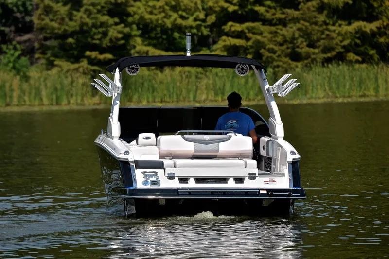 Slide: The Image of 2020 Chaparral 25 Surf boat cruising on a calm lake with lush greenery. - 10