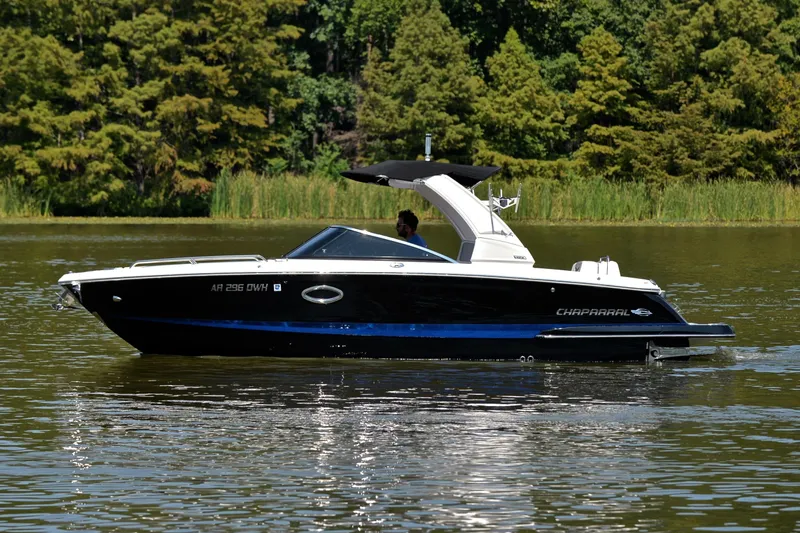 Slide: The Image of 2020 Chaparral 25 Surf boat cruising on a calm lake with lush greenery. - 11