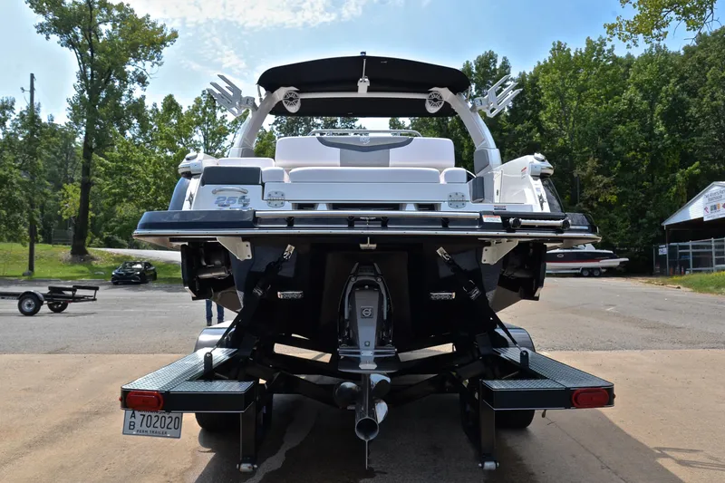 Slide: The Image of 2020 Chaparral 25 Surf boat rear view, parked on a trailer, surrounded by trees. - 15