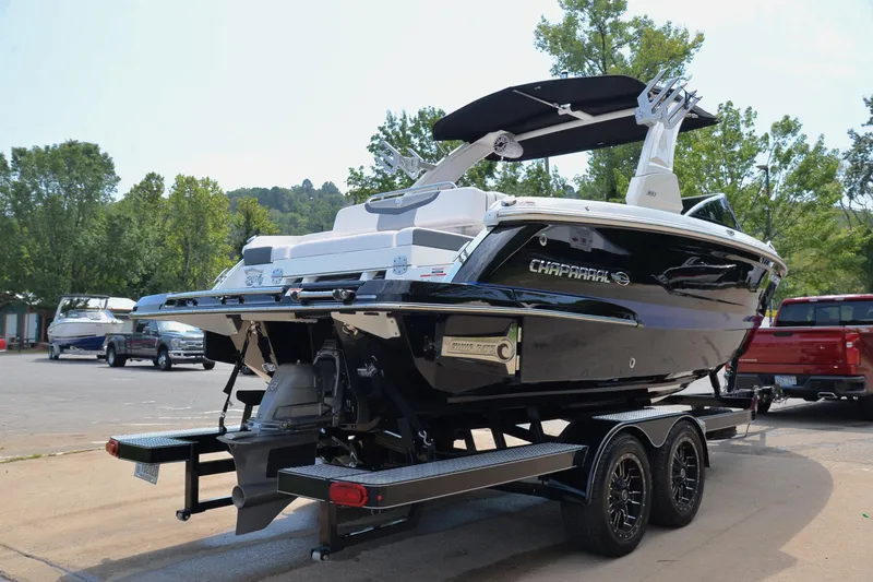 Slide: The Image of 2020 Chaparral 25 Surf boat on trailer, parked outdoors with trees in background. - 16