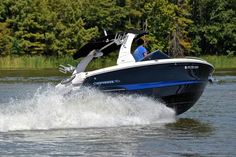Slide: The Image of 2020 Chaparral 25 Surf boat cruising on a lake with lush green trees. - 6