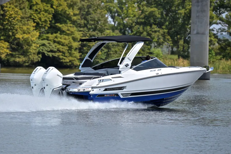 Slide: The Image of 2024 Monterey 305 Super Sport boat cruising on a calm lake with lush greenery. - 5