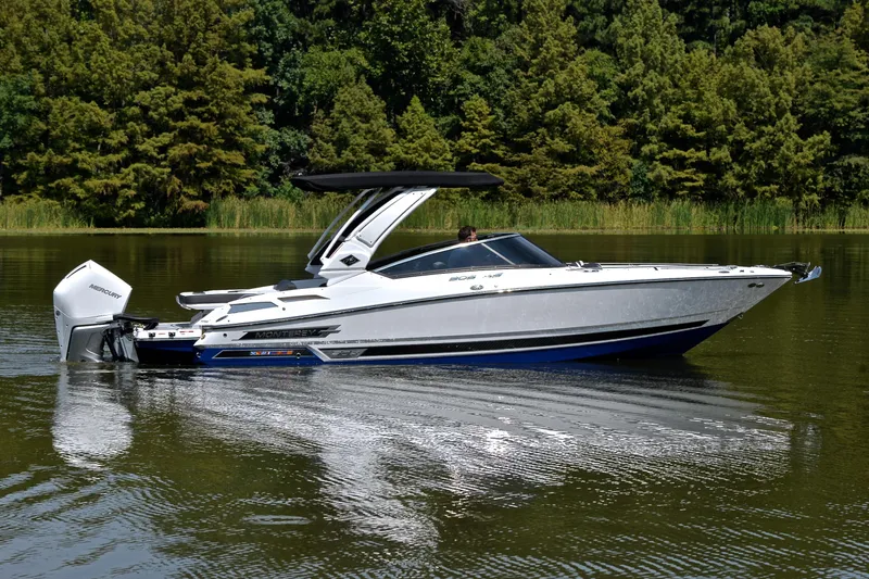 Slide: The Image of 2024 Monterey 305 Super Sport boat cruising on a calm lake surrounded by lush greenery. - 9